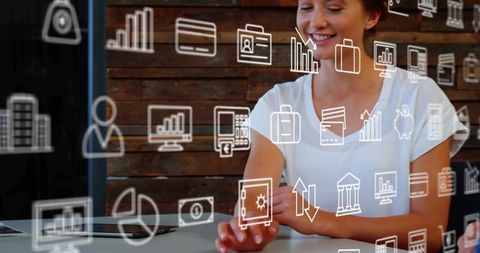 Woman tapping floating digital icons over laptop in coworking workspace
