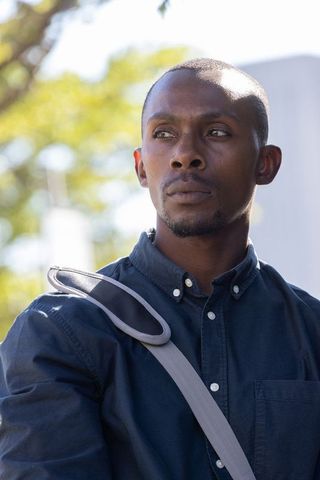 Contemplative african man standing in navy shirt with crossbody bag looking left