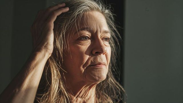 Senior woman gazing through window touching hair warm sunlight contemplative portrait