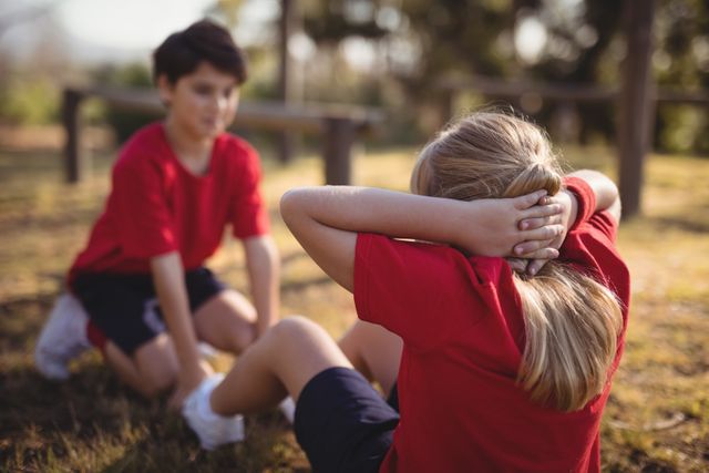 Children participating in an outdoor boot camp, performing stretching exercises. Ideal for use in content related to children's fitness, outdoor activities, teamwork, and promoting a healthy lifestyle. Suitable for educational materials, fitness programs, and summer camp promotions.