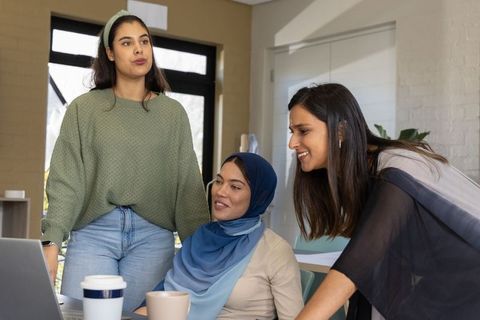 Collaborating women around laptop in bright office showing diverse muslim coworker teamwork