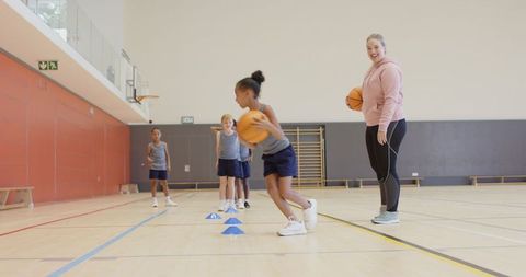 Female Coach Guiding Kids in Basketball Dribbling Practice in Gym