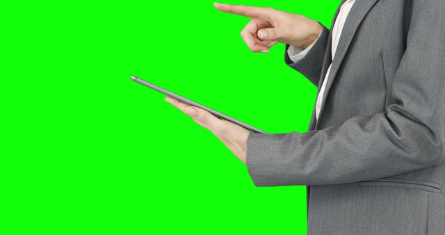 Business person holding a tablet and pointing on a green screen background. Suit jacket visible, suggesting a corporate setting. Ideal for use in business, technology, presentation, and marketing materials. The green screen allows for easy background manipulation.