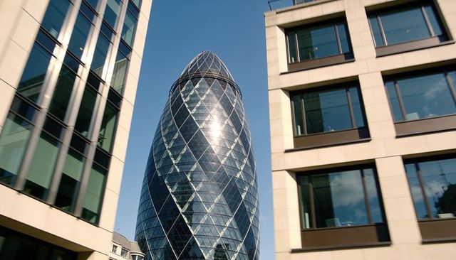 Gherkin skyscraper gleaming between glass office towers with diamond facade reflections