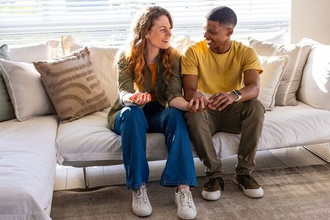 Multiracial couple sharing warm conversation holding hands on sunlit living room sofa