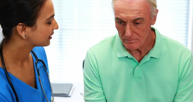 Friendly doctor in blue scrubs discussing health with elderly man. Can be used in health care articles, clinic brochures, medical websites emphasizing compassionate care, doctor-patient relationship, and senior health.