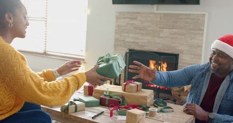 Couple wrapping holiday gifts by fireplace, cozy living room gift exchange