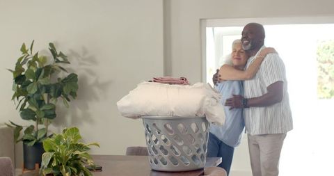 Senior Couple Sharing Loving Hug in Cozy Home Near Laundry Basket
