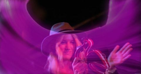 Musician in hat with tambourine under vibrant purple lights