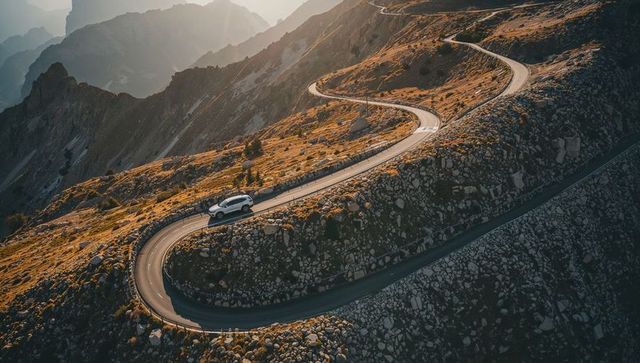 White suv climbing winding alpine switchback road at high mountain pass, aerial view