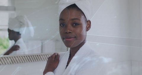 Serene woman in white bathrobe and towel turban at bathroom mirror, skincare routine