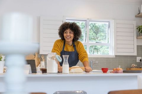 African american woman kneading dough on sunlit kitchen island wearing denim apron