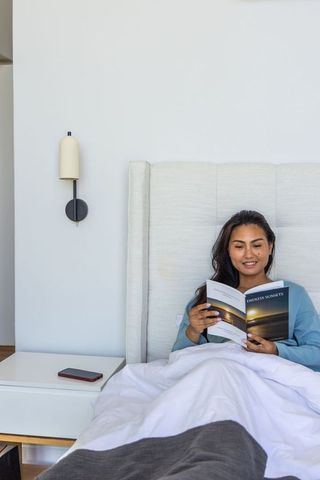 Asian woman reading in bed in minimalist modern bedroom with smartphone on nightstand