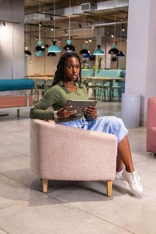 African american woman working on tablet in modern pastel coworking lounge with plants
