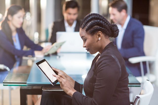 Businesswoman using digital tablet while colleagues work in background. Suitable for business, tech, and corporate collaboration themes.