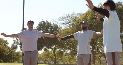 Diverse men performing arm warm-ups in sunlit park for outdoor fitness routine