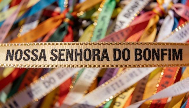 Gold-trimmed nossa senhora do bonfim ribbon amid multicolor devotional fitinhas, salvador brazil