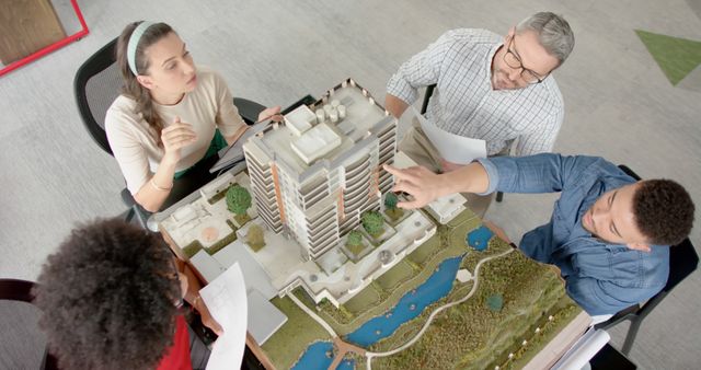 Group of architects gathered around a detailed building model, discussing and collaborating on a project. Ideal for content related to architectural design, team collaborations, project planning, and office environments.