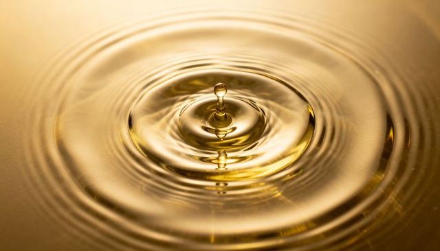 Golden water droplet creating vertical splash and concentric ripples, macro liquid detail