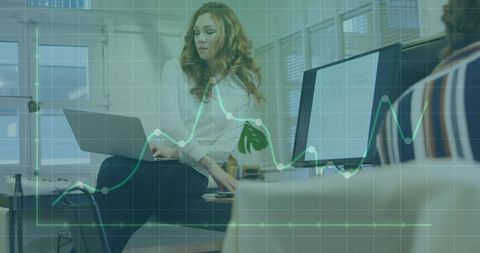Female professional working on laptop with analytics overlay in modern open office team