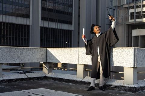 African american graduate taking selfie on urban rooftop with diploma