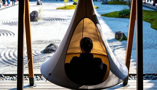 Woman relaxing in cocoon pod over japanese rock garden on sunlit wooden deck