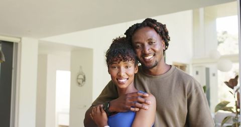 African couple embracing at home smiling wearing fitness tracker and casual activewear