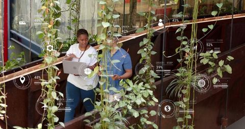 Collaborating in biophilic atrium with laptop and phone displaying hud analytics