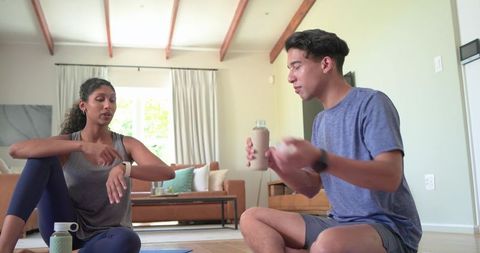 African-american couple hydrating and checking smartwatch after home workout in sunlit room