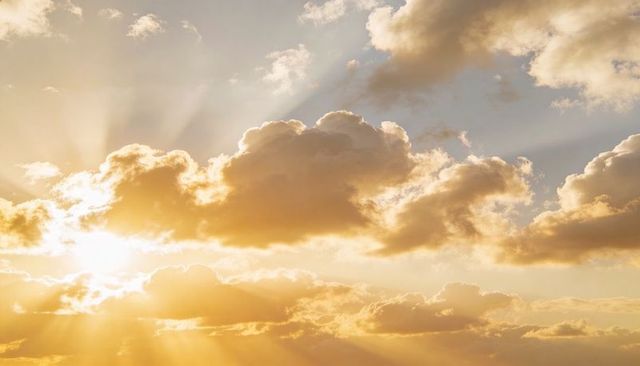 Golden sunrise rays glowing through cumulus clouds, crepuscular sunbeams lighting horizon
