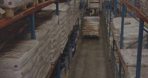 Forklift moving pallet through warehouse aisle among stacked goods