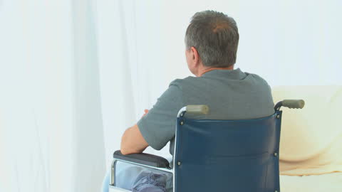 Rear View of Man in Wheelchair with Contemplative Expression Facing Window