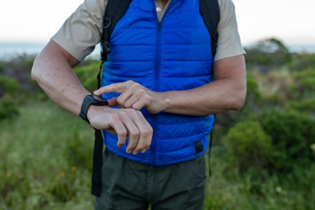 Senior man hiking in the mountains, using a smartwatch to track his progress. Ideal for promoting outdoor activities, fitness technology, and active lifestyles for seniors. Can be used in advertisements for smartwatches, hiking gear, or health and wellness campaigns.