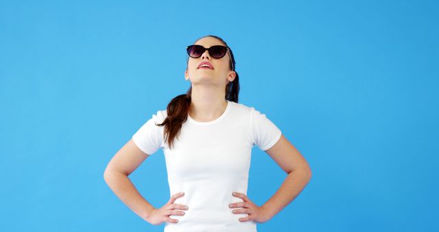 Young Woman Wearing Sunglasses Looking Up Against Blue Background - Download Free Stock Images Pikwizard.com