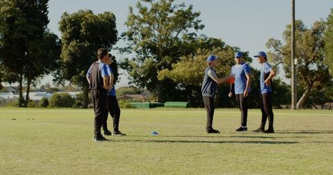 Youth football team practicing passing drill with coach holding red ball on park field