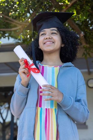 African american teen graduating wearing mortarboard holding diploma outdoors