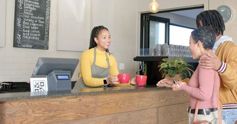 Smiling barista serving coffee to affectionate african american couple at cozy cafe counter