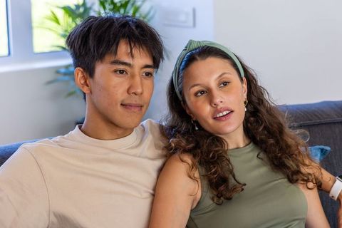 Young diverse couple relaxing on sunlit living room sofa sharing quiet moment at home