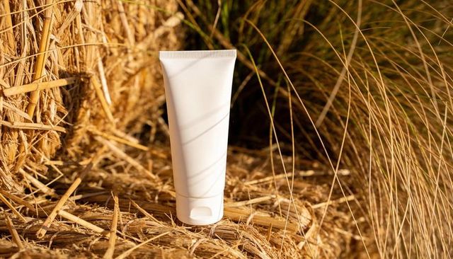 White squeeze tube on golden hay bale catching sunlight for eco rustic packaging mockup