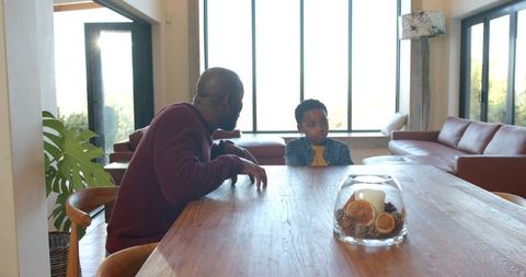African american father and son having quiet heartfelt conversation at modern dining table
