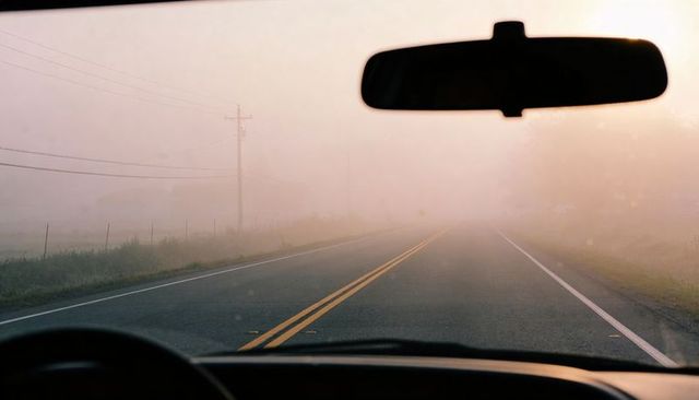 Driving into morning fog on rural two-lane road viewed through windshield, rearview mirror