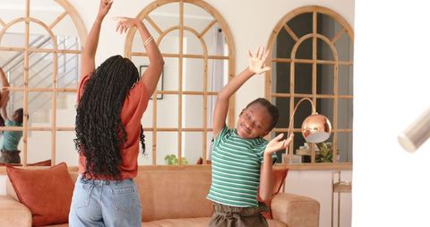 African woman and girl dancing and stretching in cozy living room with arched mirrors