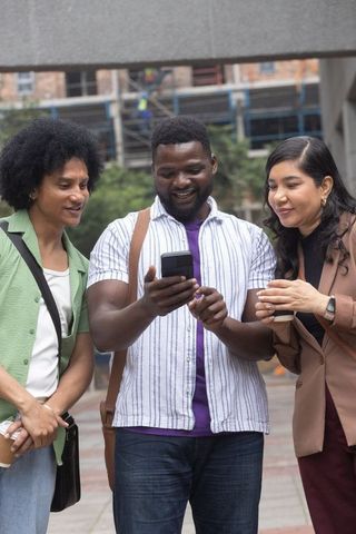 Multicultural friends sharing smartphone and coffee in urban plaza