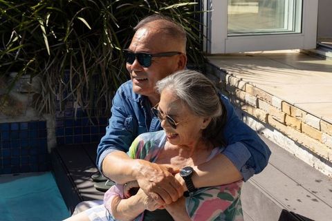 Sunlit senior couple embracing on patio, enjoying poolside romance and companionship