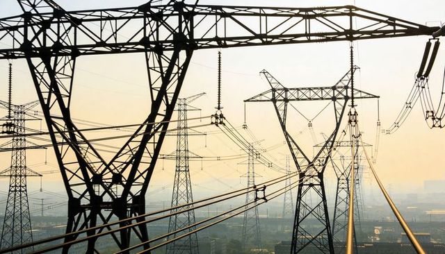 High-voltage transmission towers supporting power lines over industrial landscape at dawn