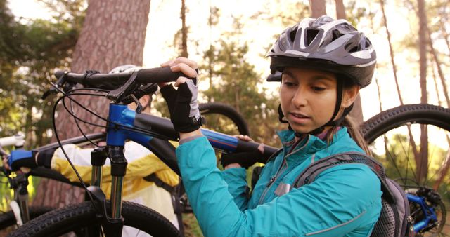 A young Asian woman adjusts her bicycle helmet in a forest setting, with copy space. Her focus and attire suggest she is preparing for a mountain biking adventure.