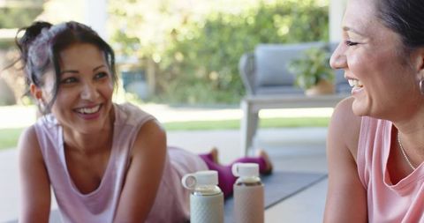 Smiling friends resting after outdoor workout on patio with mats and water bottles