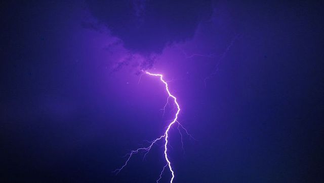 Electric lightning bolt illuminating night sky with purple clouds