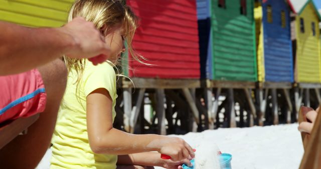 Young girl playing with sand near colorful beach huts on a sunny day - Download Free Stock Images Pikwizard.com