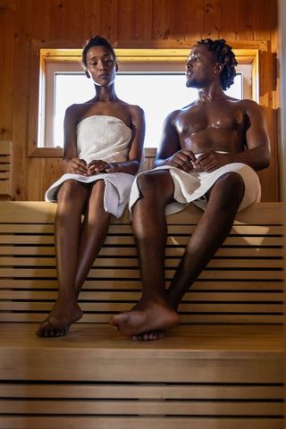African american couple relaxing in wood sauna, towels, sweating, backlit intimate moment